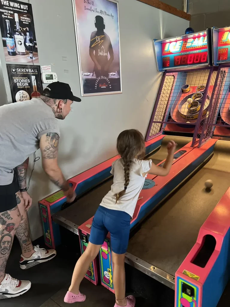 Man and girl play 'ICE BALL' arcade game, girl throwing ball.