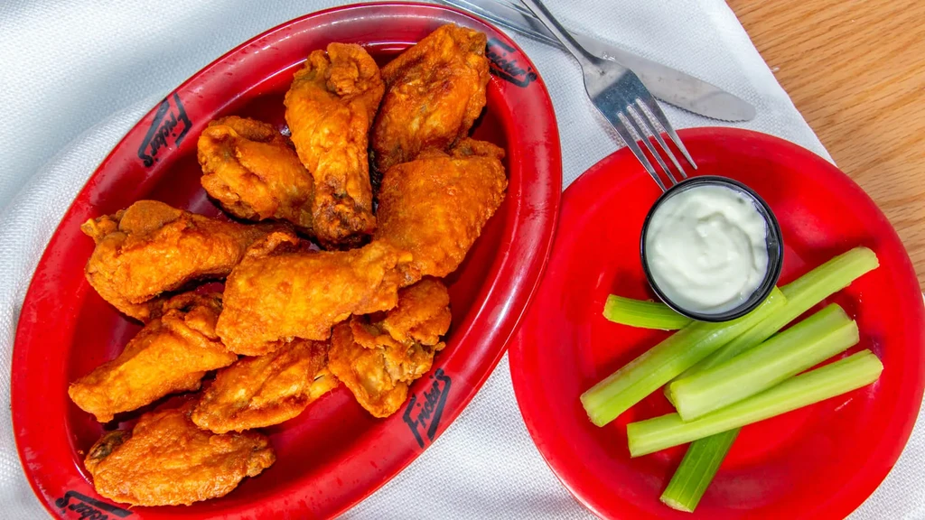 Fried chicken wings, celery, and dipping sauce on Fricker's red plates.