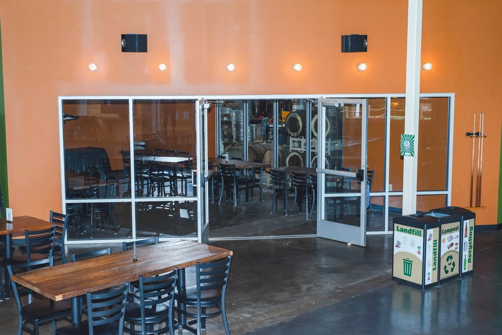 Orange-walled brewpub dining room overlooks industrial brewery production area.