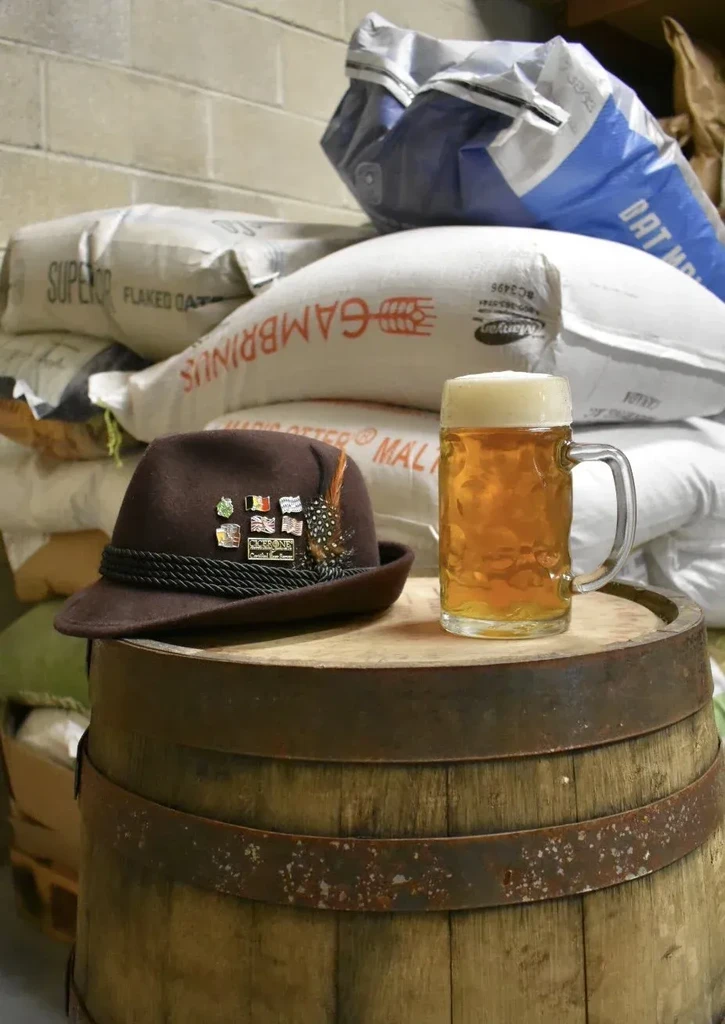 Golden beer mug, Tyrolean hat, and malt bags on a wooden barrel.