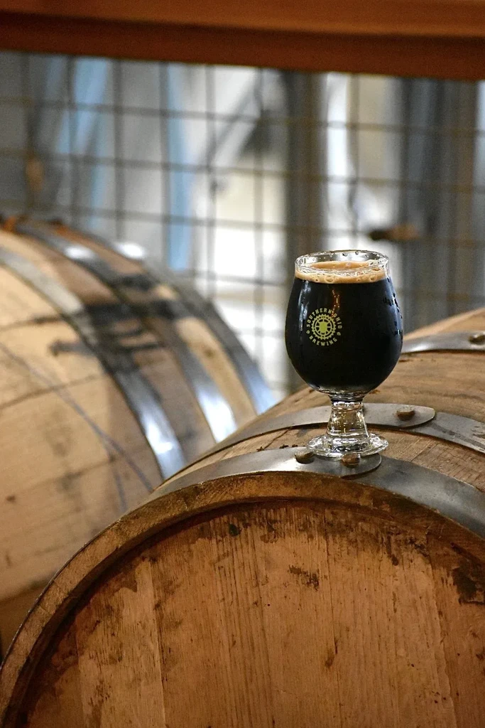 Glass of cold dark beer on a wooden barrel in a brewery.