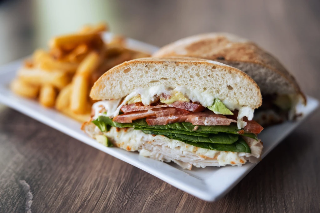 Half sandwich with turkey, cheese, avocado, vegetables, and fries.