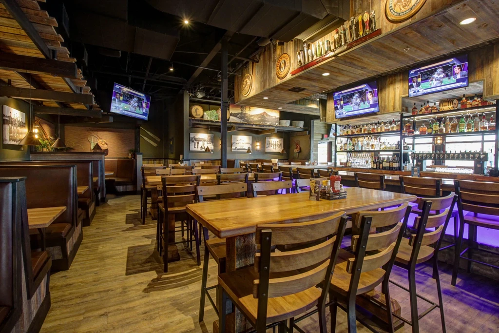 Empty, rustic-industrial sports bar interior with wood, TVs, and a stocked bar.