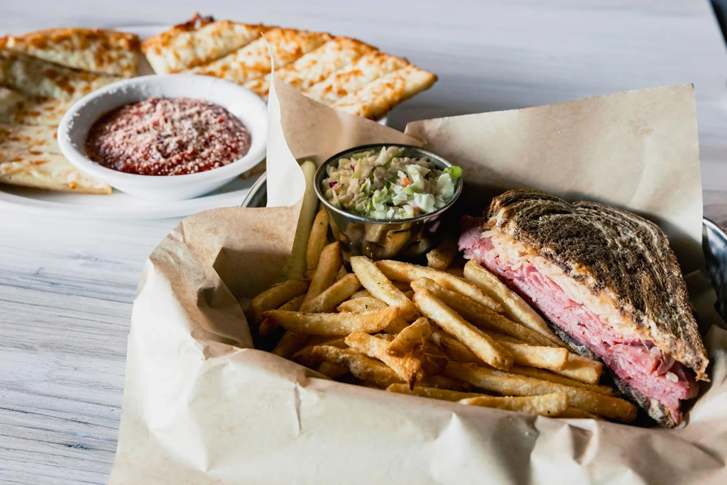 Close-up of a Reuben sandwich, fries, and coleslaw in a basket.