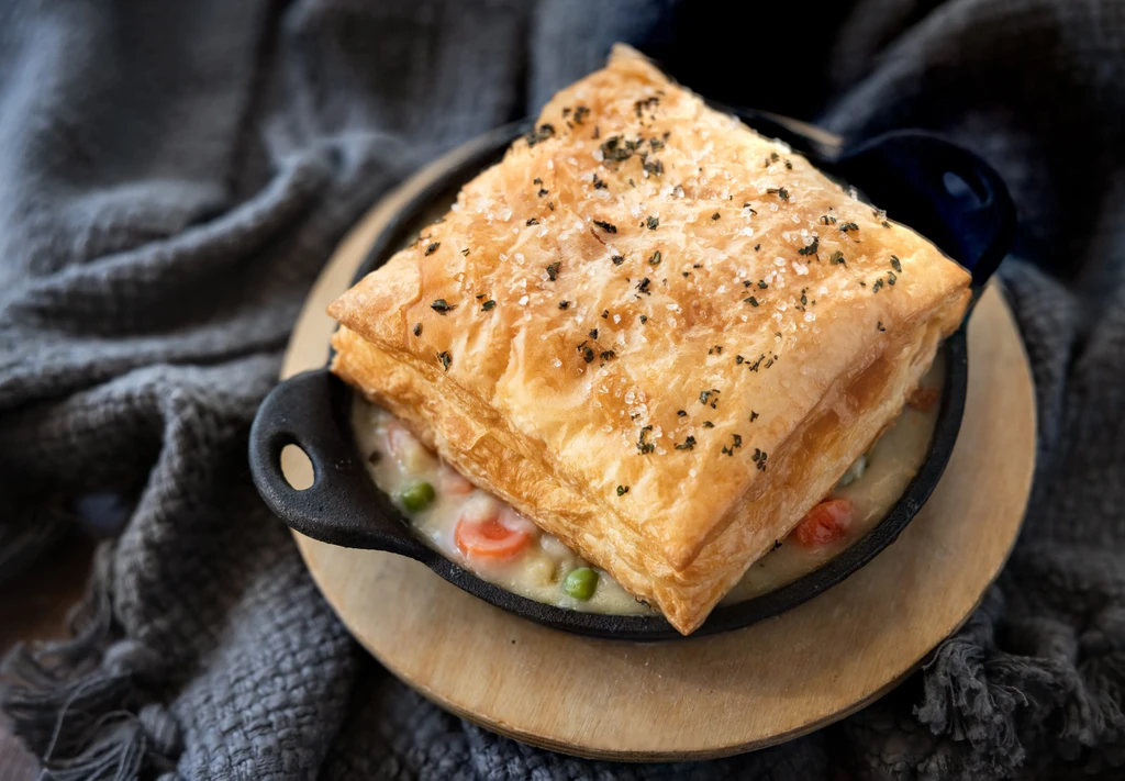Savory chicken pot pie in skillet, flaky golden pastry, carrots, peas.
