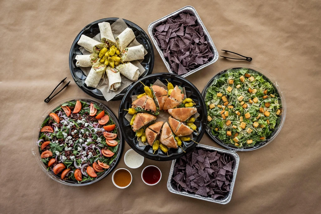Overhead view of a diverse catering spread with wraps, salads, and chips.