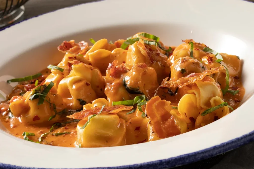 Creamy tortellini pasta topped with herbs, crispy bacon, and chili flakes.