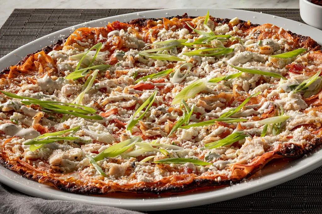 Close-up savory flatbread with chicken, crumbled feta, creamy sauce, scallions.