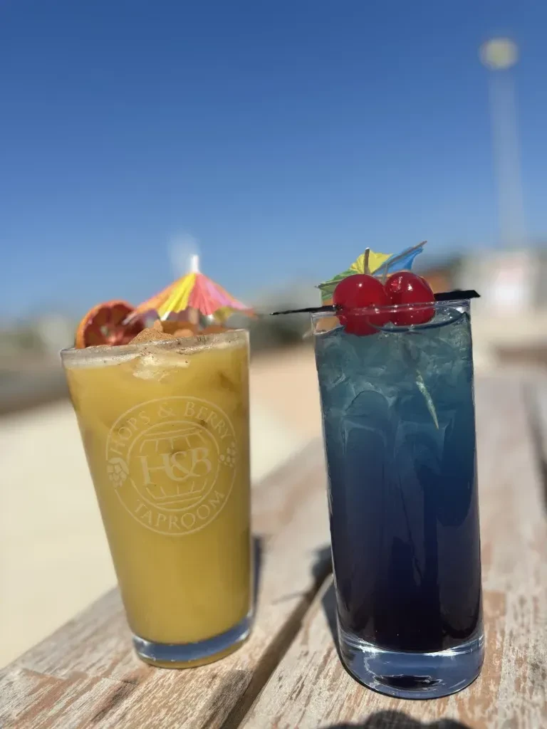 Two colorful cocktails with umbrellas on wood against a blue sky.
