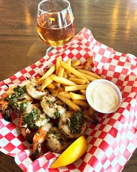 Overhead shot of grilled shrimp and fries basket with beer on a table.