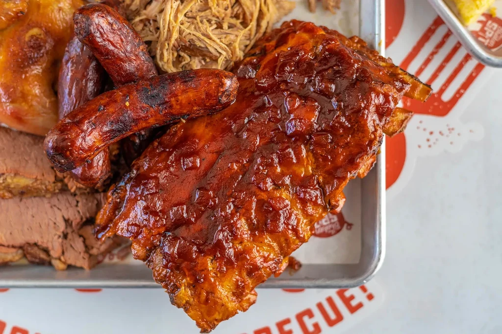 Platter with sauced ribs, charred sausages, pulled pork, and brisket slices.