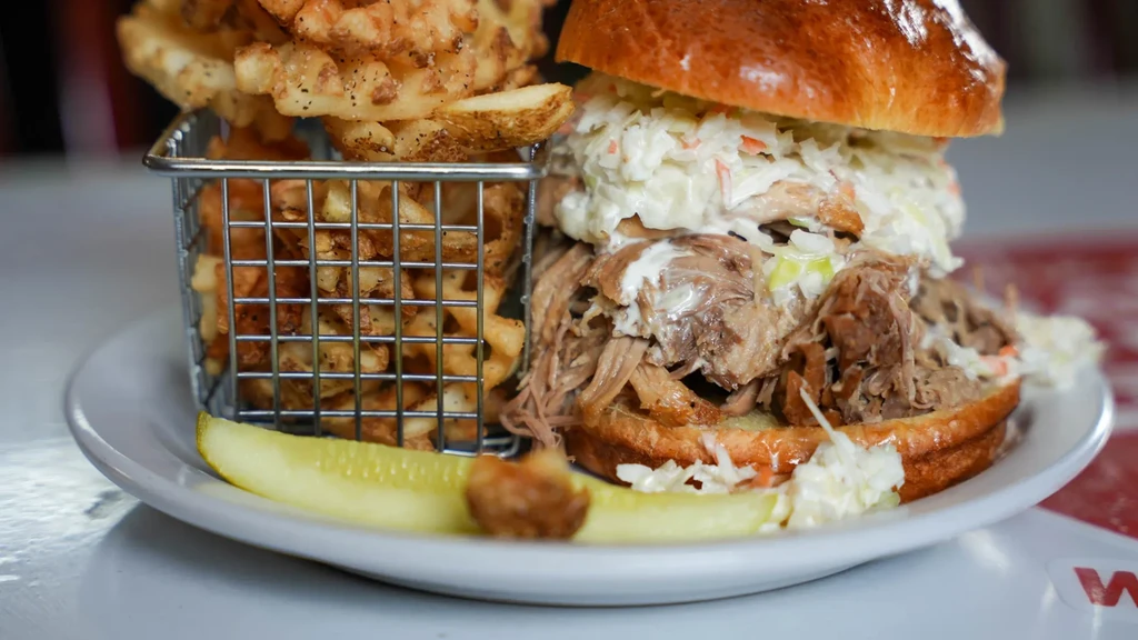 Pulled pork sandwich with coleslaw, waffle fries, and a pickle spear.
