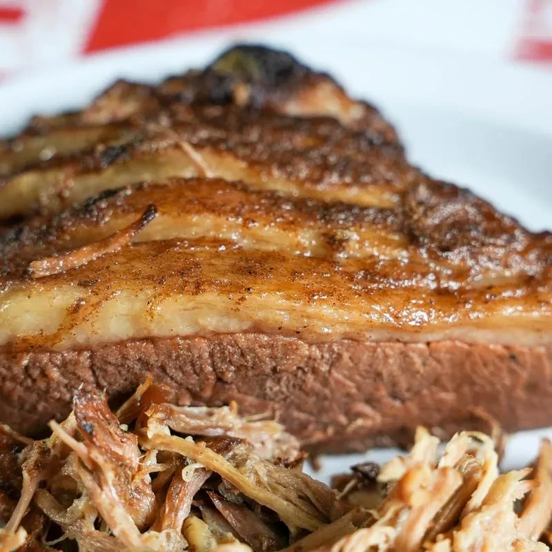 Close-up: Roasted meat with crispy crust, rendered fat, and pulled meat.