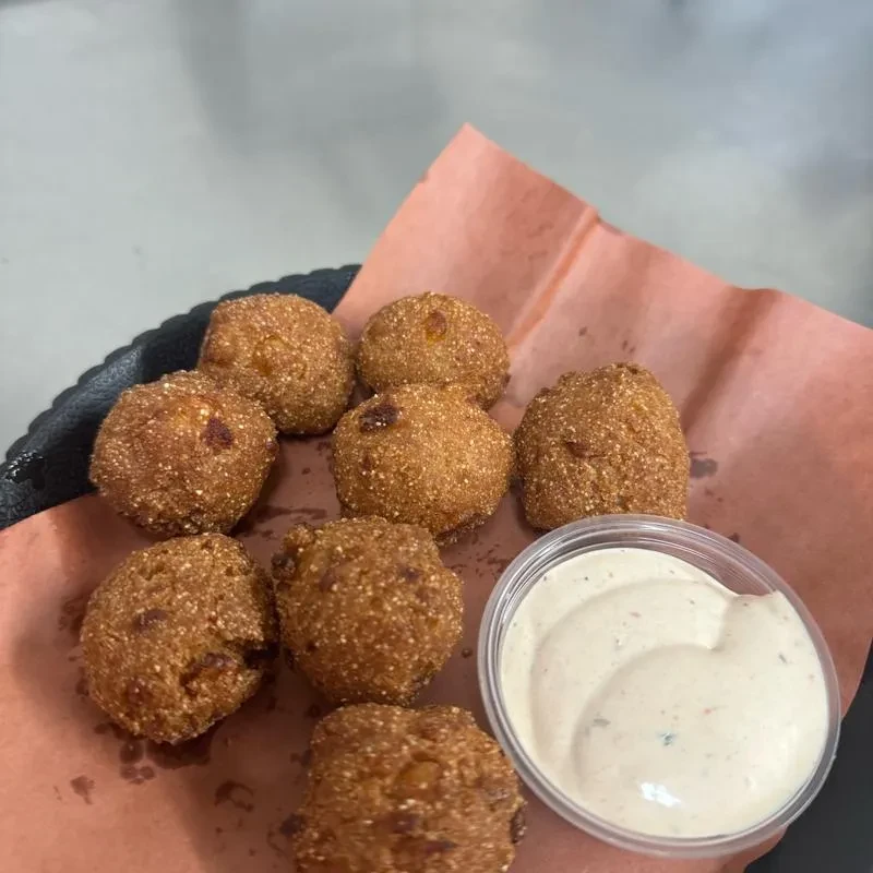 Golden-brown hushpuppies on butcher paper with creamy dipping sauce.