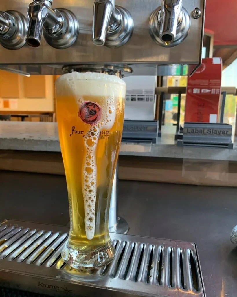 Golden beer in a tall glass, frothy head and lacing under taps.