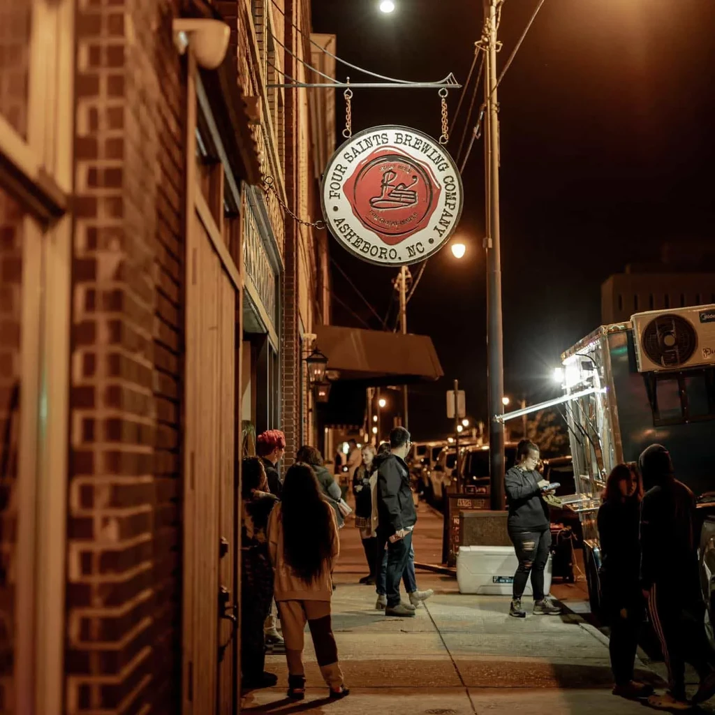 Night view of Four Saints Brewing Co. with people and food truck.