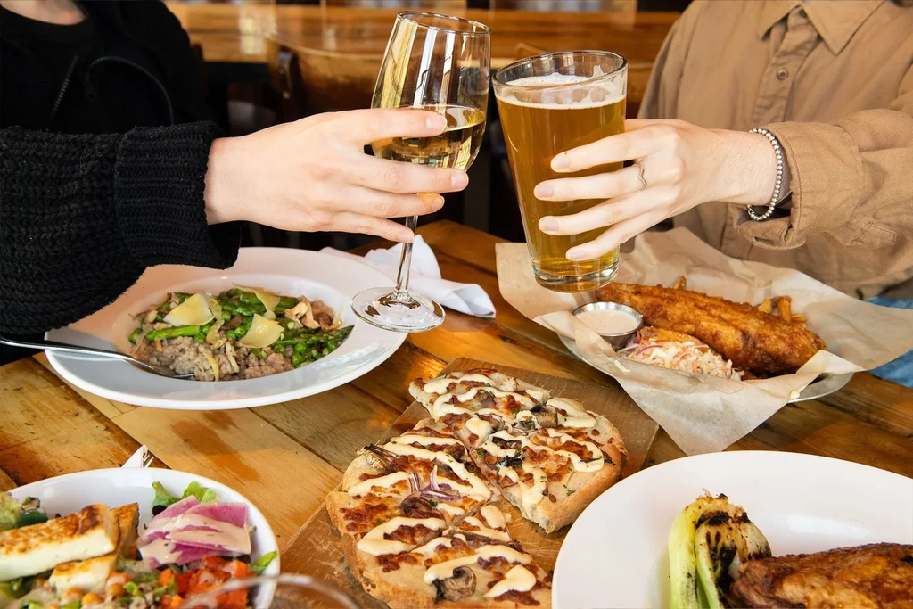 High-angle view: restaurant table with diverse food, two people toasting.
