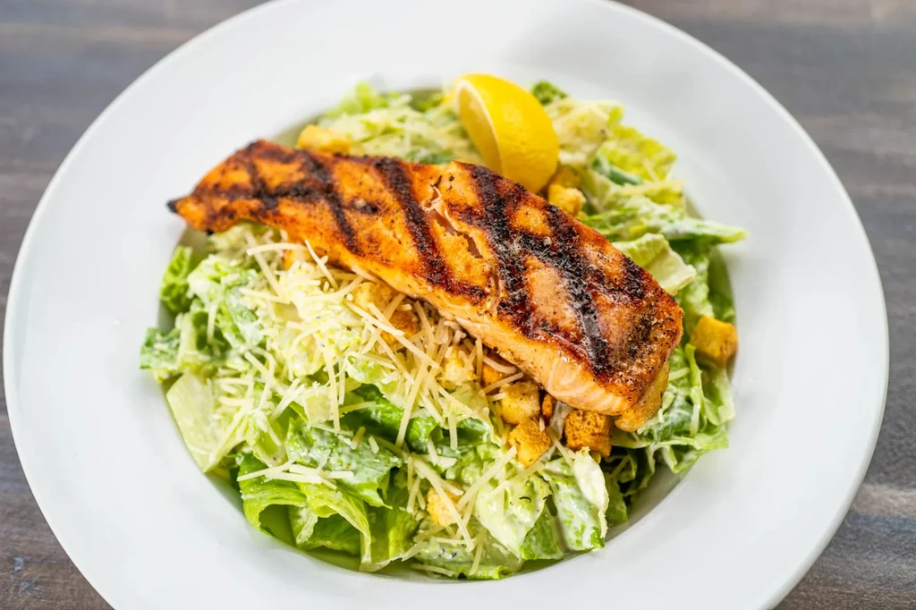 Grilled salmon Caesar salad with lemon on a white plate.