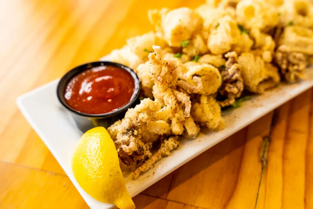 Close-up of golden-brown fried calamari, red sauce, and lemon wedge.