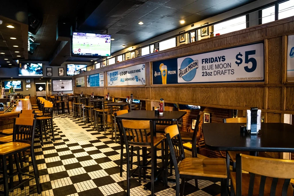 Empty sports bar with checkerboard floor, wooden walls, and TVs.