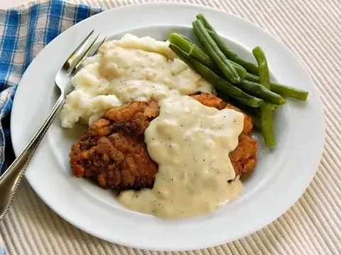 Plate of gravy-covered fried meat, mashed potatoes, and green beans.