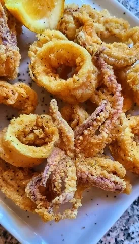 Rectangular plate of golden-brown fried calamari, garnished with a citrus wedge.
