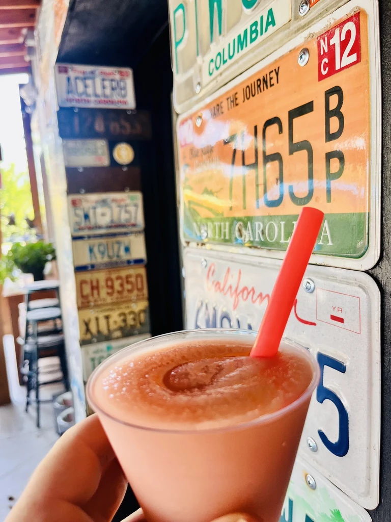 Close-up of frozen coral drink with red straw against license plate wall.