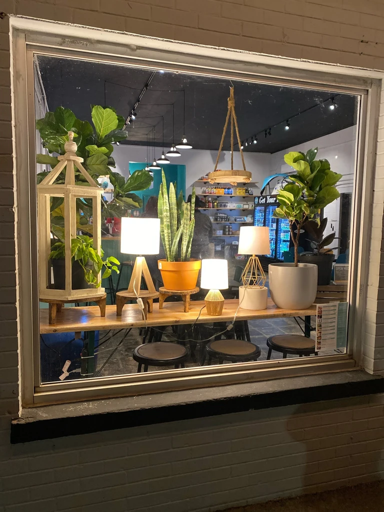Cafe window display at night, featuring potted plants and lit lamps.