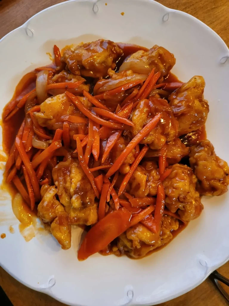 Top-down chicken dish with glossy orange sauce, carrots, onions.