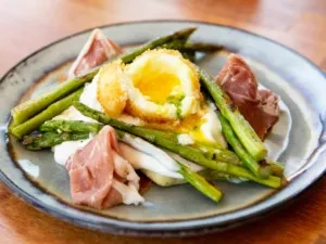 Fried egg with runny yolk, asparagus, prosciutto on a rustic plate.