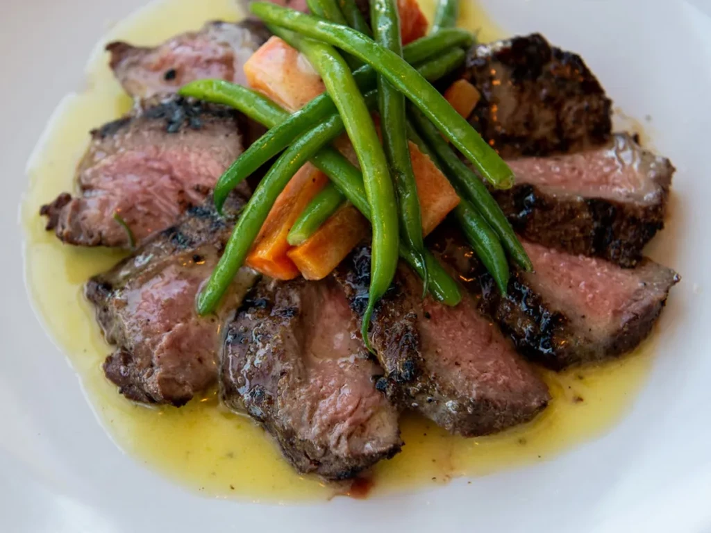 Medium-rare steak, green beans, orange vegetables, and yellow sauce.