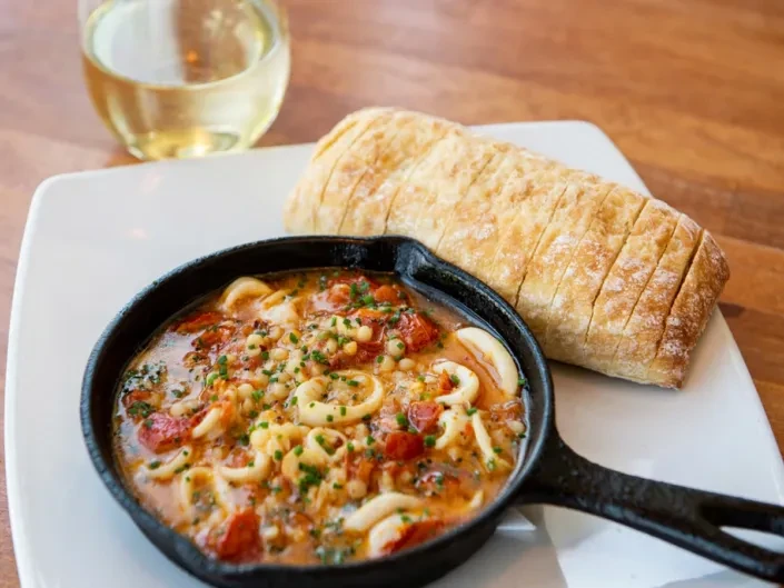 Calamari, tomato, and pasta stew in rustic skillet with bread.