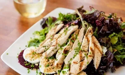 Grilled chicken salad with eggs, chives, and mixed greens on white plate.