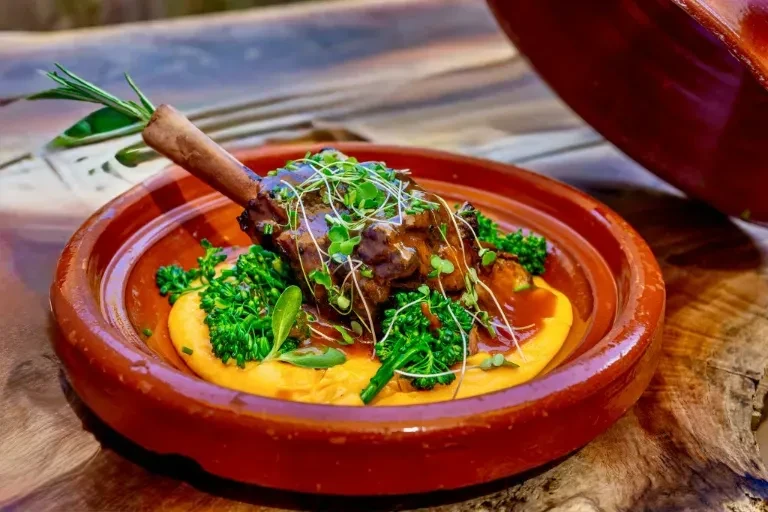 Braised meat on bone with puree and greens in rustic bowl.