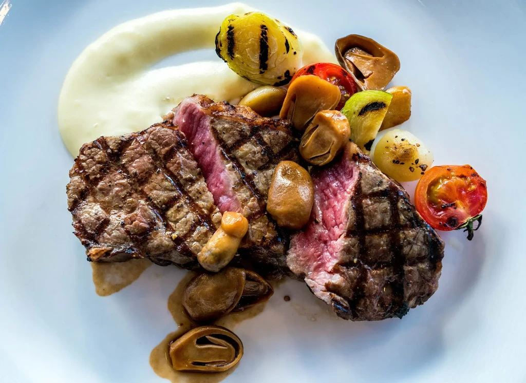 Meticulously plated grilled steak, medium-rare, with vegetables, mushrooms, and sauces.