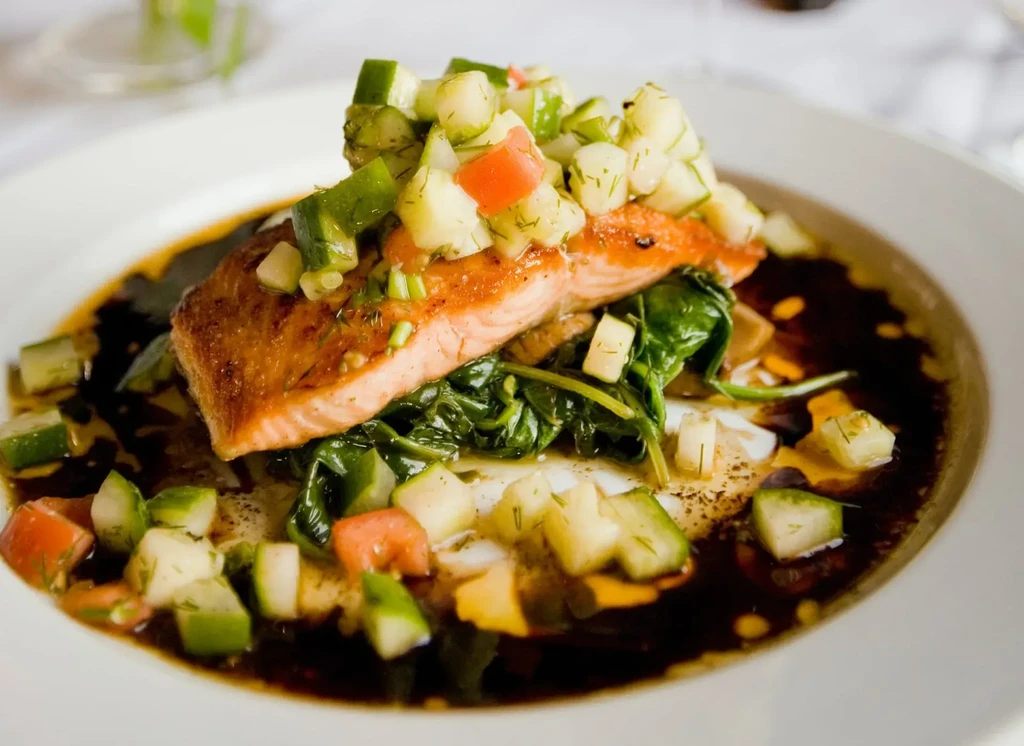 Pan-seared salmon with colorful salsa, spinach, and dark sauce on a plate.
