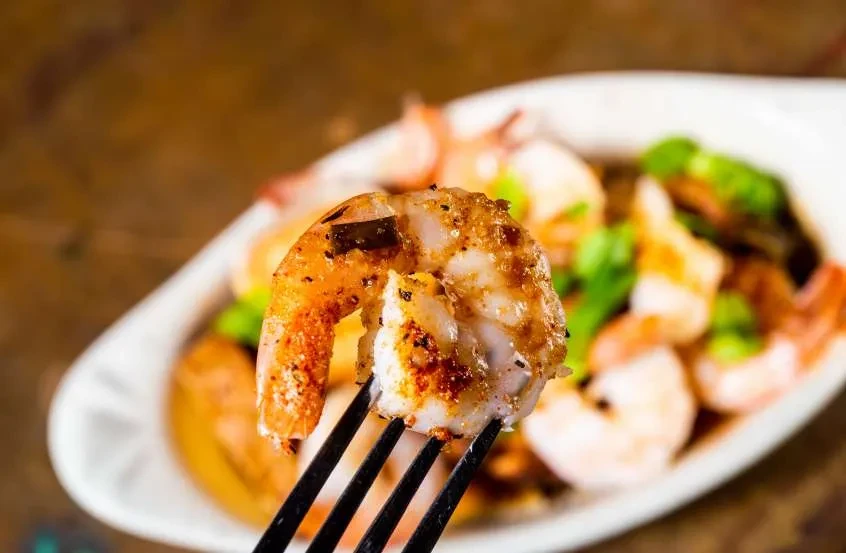 Cooked seasoned shrimp on a fork, with more in a dish.