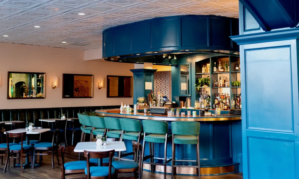 Restaurant interior with a prominent teal bar and empty dining area.