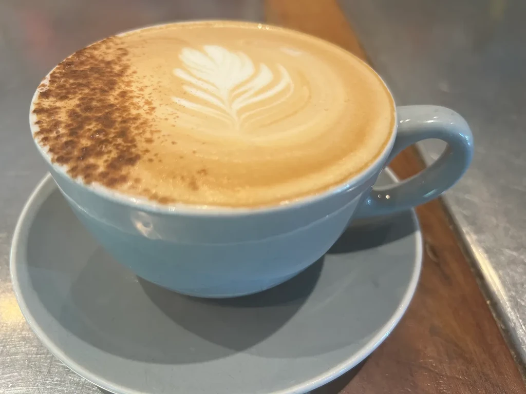 Close-up of cappuccino in blue cup with leaf latte art, dusted powder.