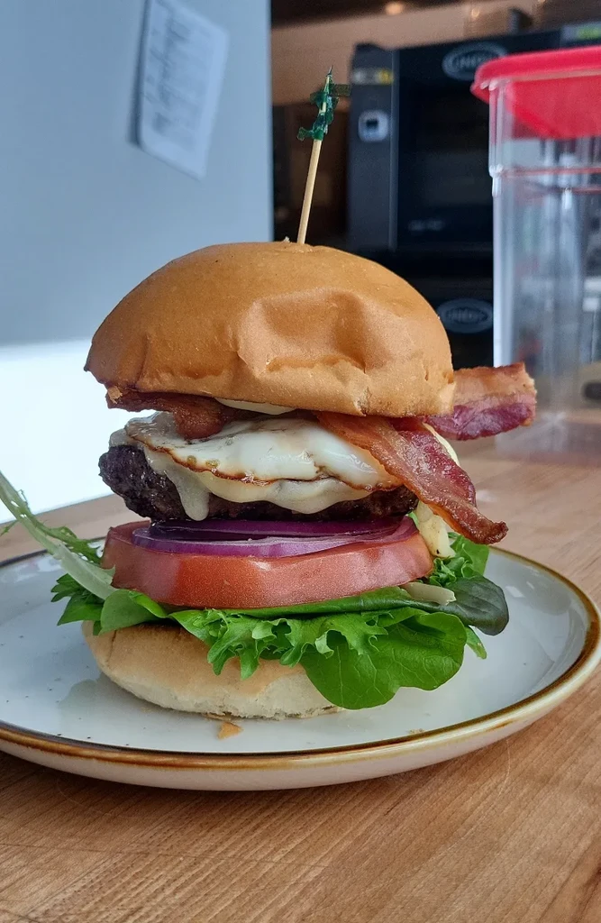 Close-up of a tall burger with egg, bacon, and a toy soldier toothpick.