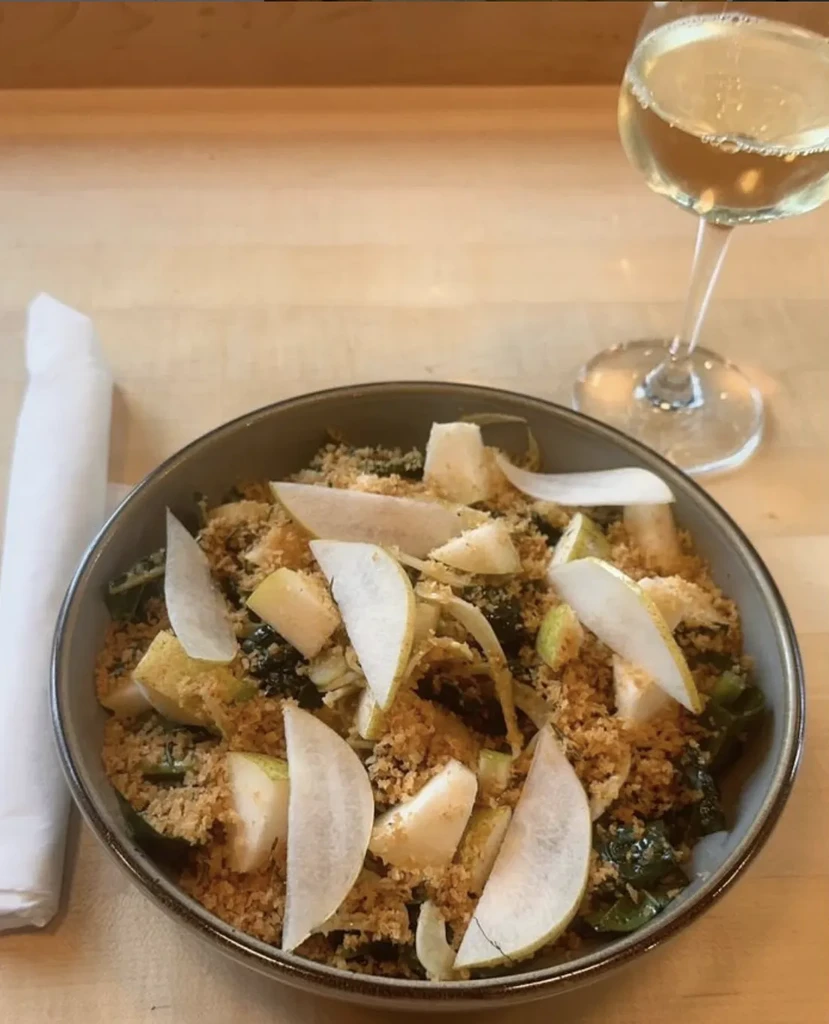 Garnished salad bowl, golden topping, white wine on wooden table.