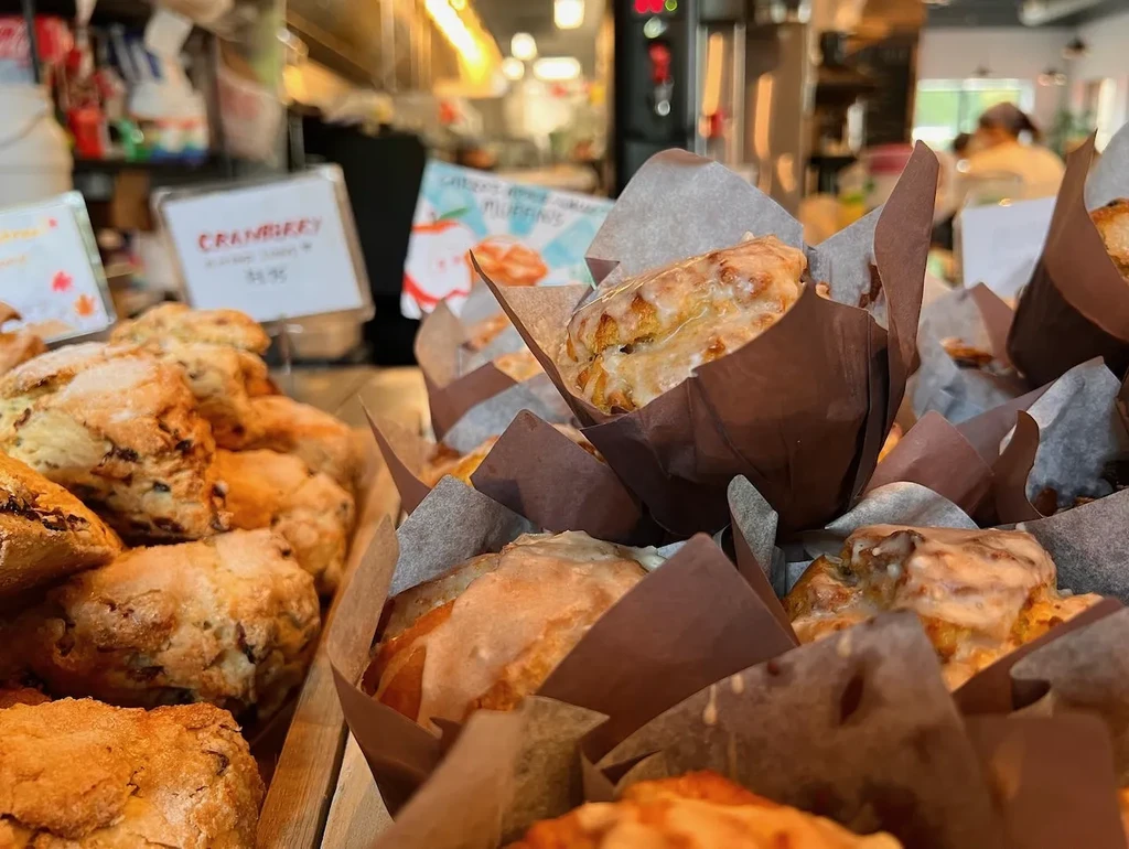 Close-up of glazed pastries and scones on a bakery counter with signs.