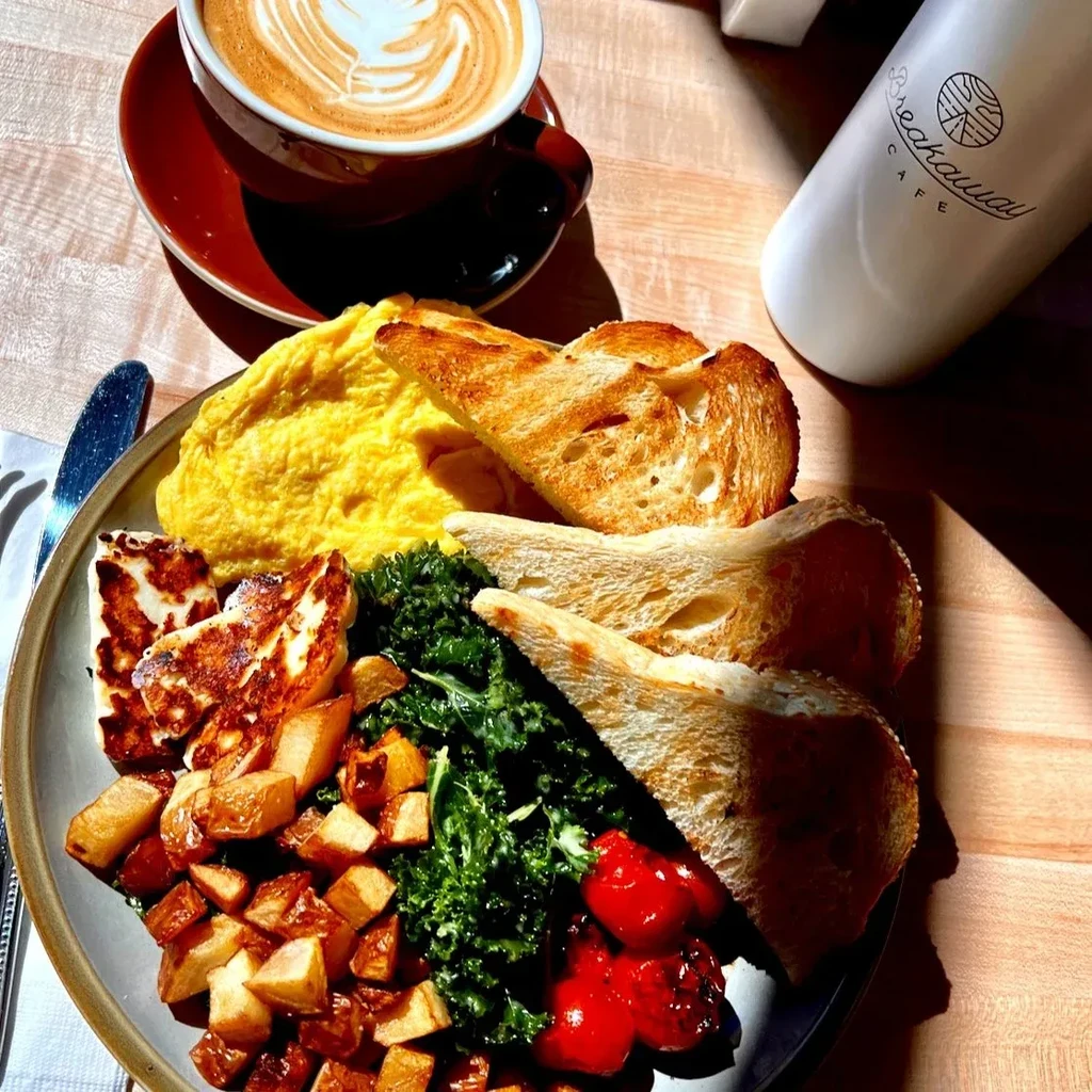 Overhead: Cafe breakfast plate with eggs, halloumi, greens, potatoes, and latte.