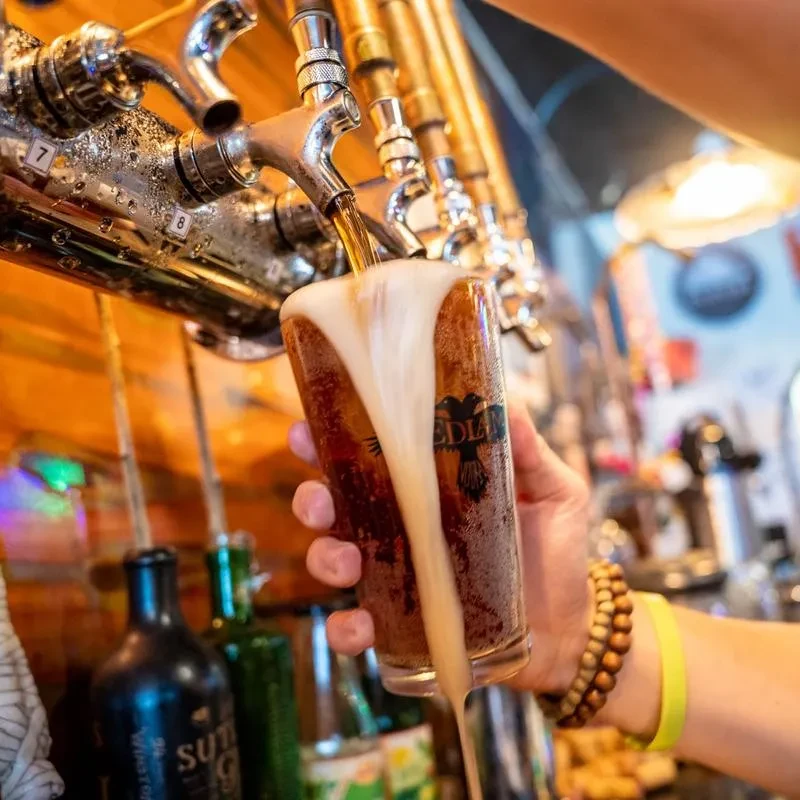 Hand fills EDLIN glass with overflowing dark beer from a tap.