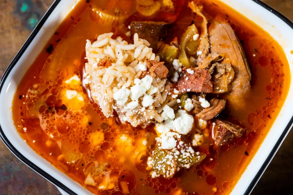 Close-up of a hearty stew with rice, crumbled cheese, and meat.