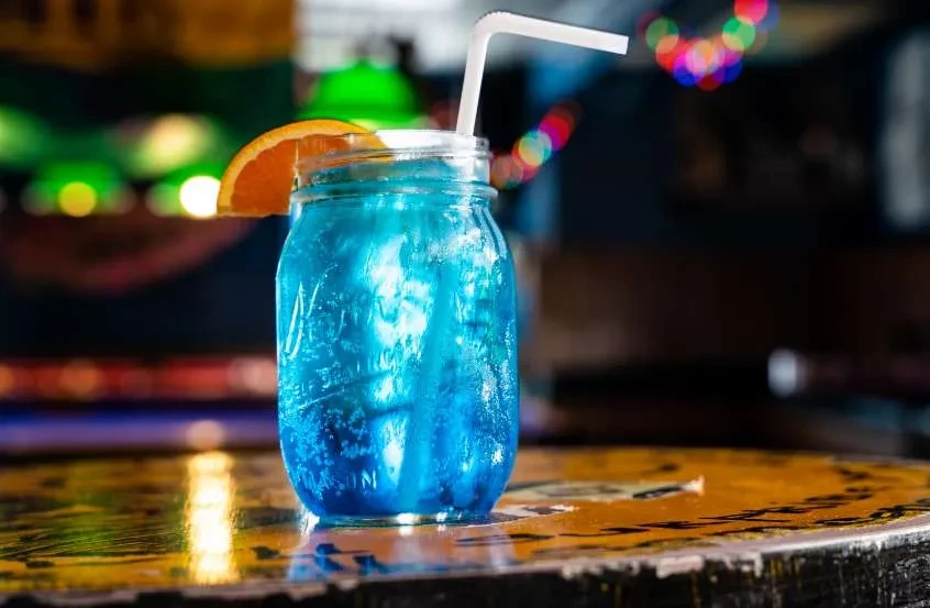 Blue cocktail in a mason jar with orange and blurred colorful lights.
