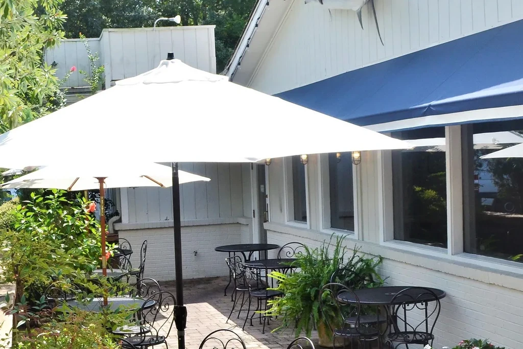 Restaurant patio with white umbrellas, tables, green plants, and a fish sculpture.