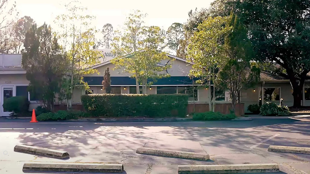 Single-story building with blue awnings, peaked roof, and asphalt parking lot.