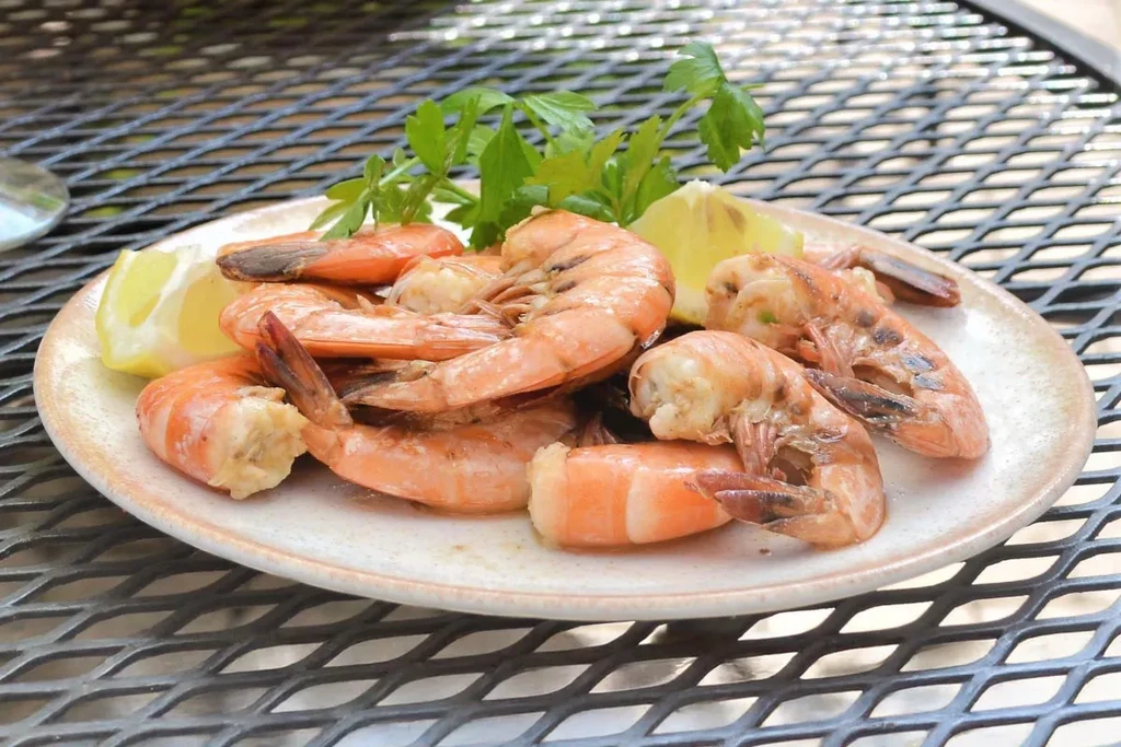 Plate of grilled shrimp garnished with lemon and parsley on a mesh table.