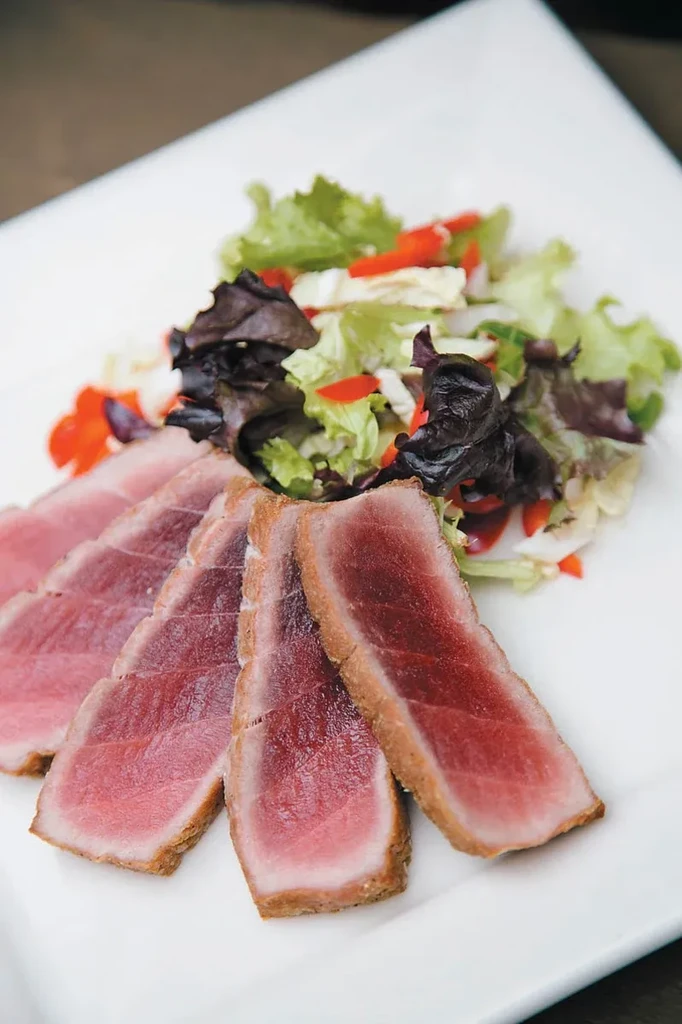 Slices of seared tuna and a fresh side salad on a white plate.